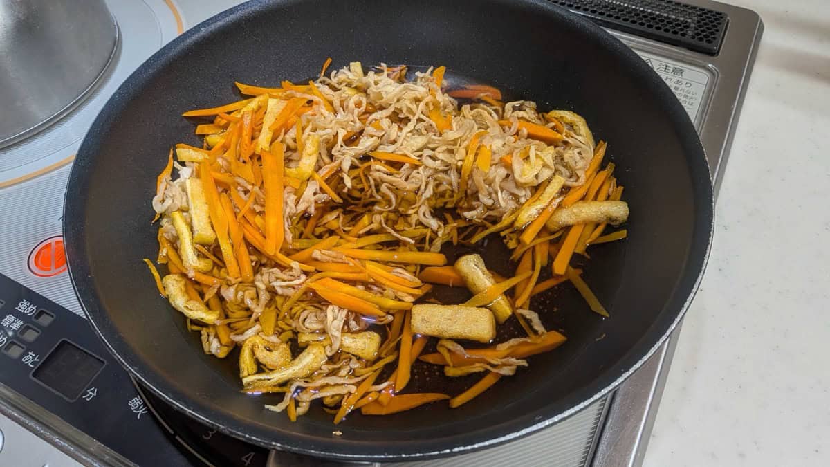 The pan filled with dark soy-dashi broth simmering with daikon, carrot and fried tofu