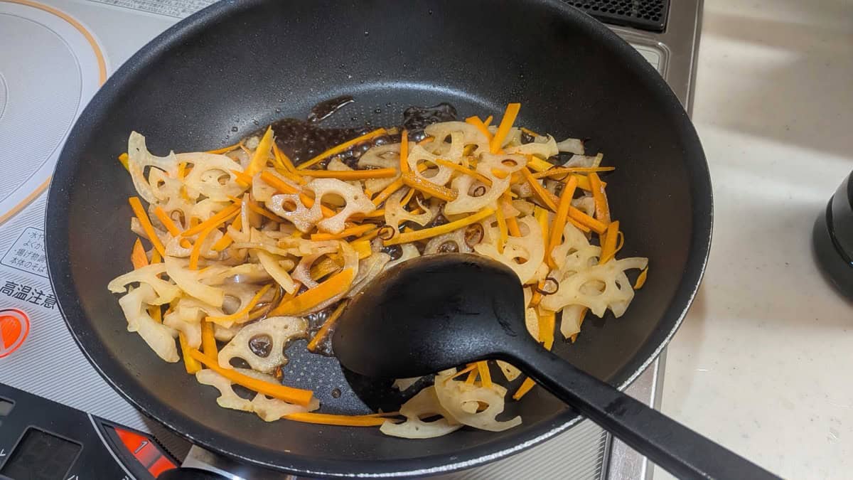 Soy sauce, mirin and sugar added to the pan of lotus root and carrot, bubbling before it reduces