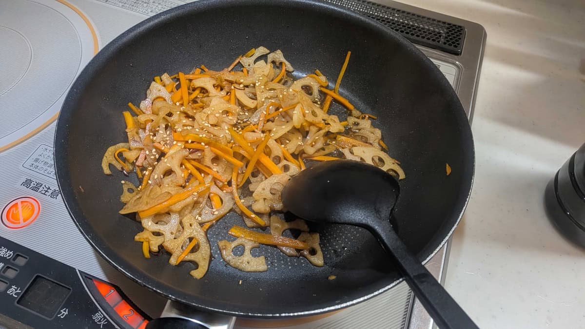 White sesame seeds scattered over the finished lotus root kinpira in the pan