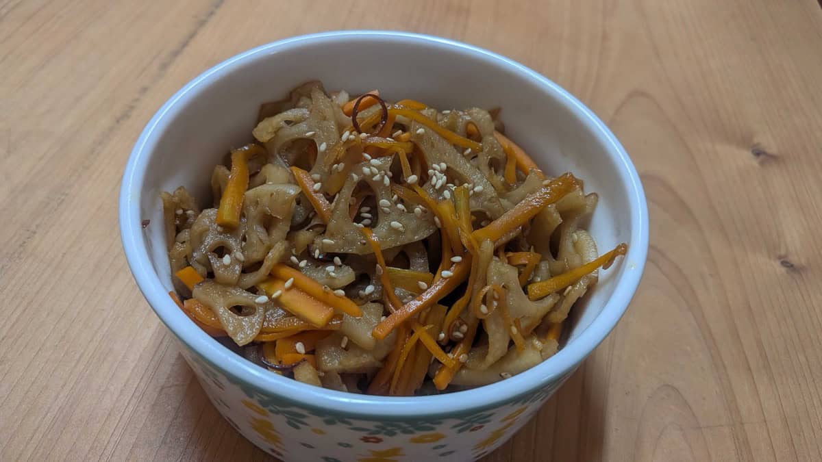 Lotus root kinpira with carrot and sesame seeds in a small bowl on a wooden table, seen from above