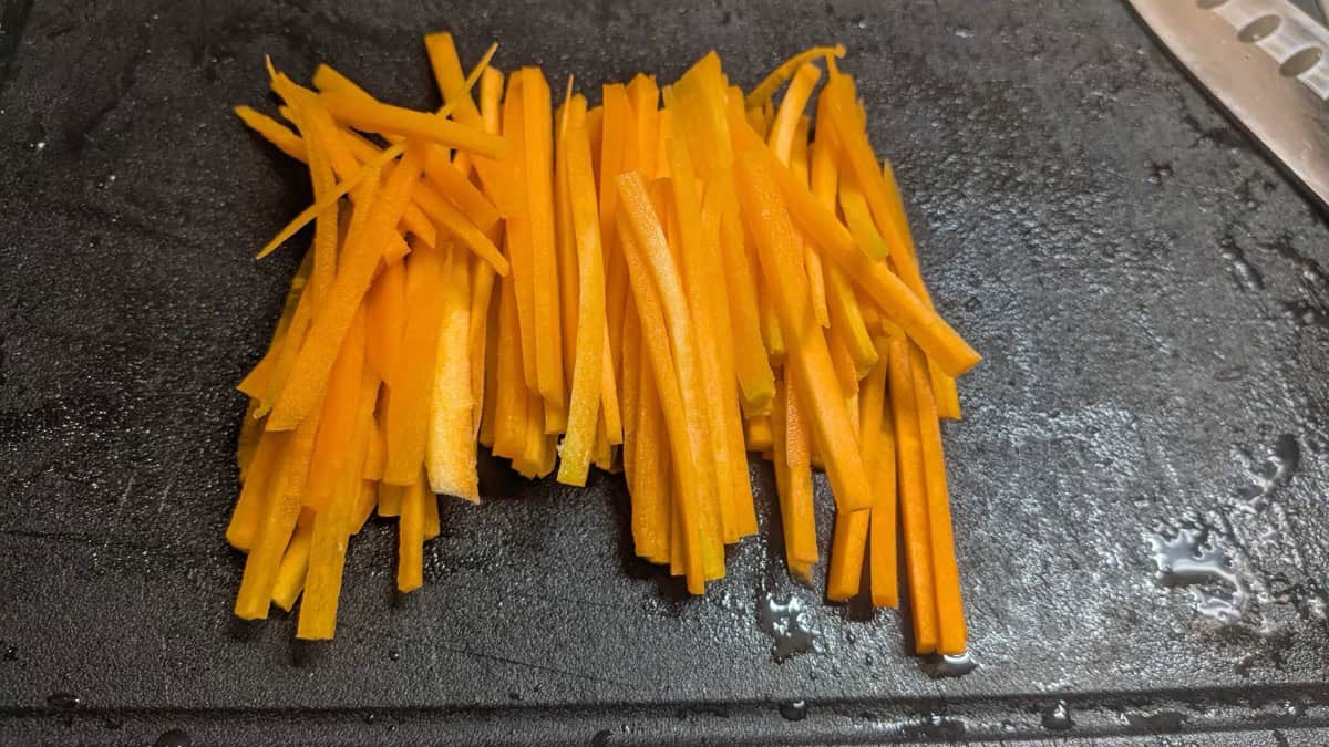 Carrot cut into thin matchsticks on a black cutting board