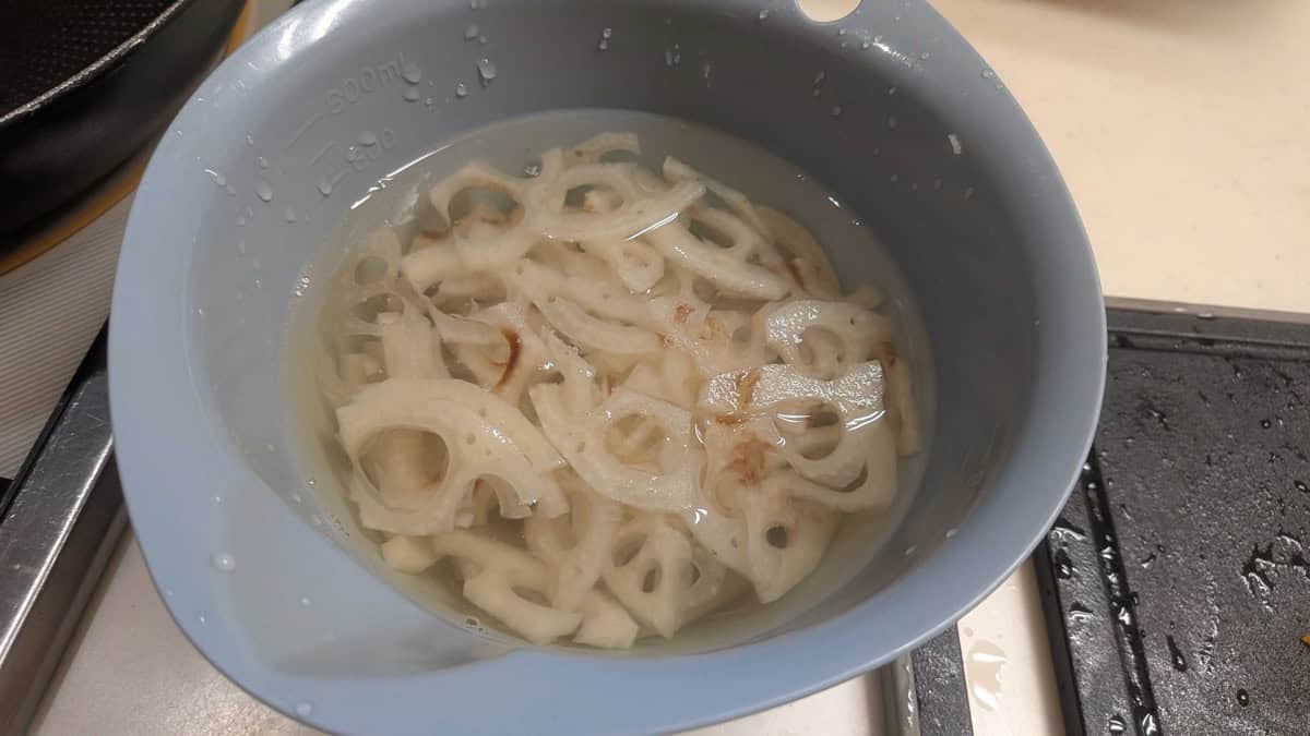 Thinly sliced lotus root soaking in a bowl of cold water, showing the characteristic holes in each slice