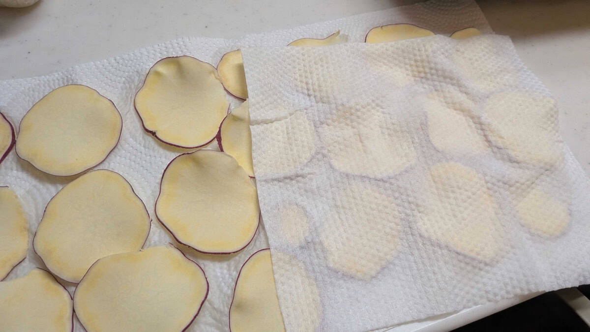 Sliced sweet potato laid out on paper towels and being patted dry before cooking