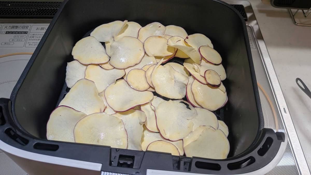 Honey-buttered sweet potato slices spread out in the air fryer basket before cooking