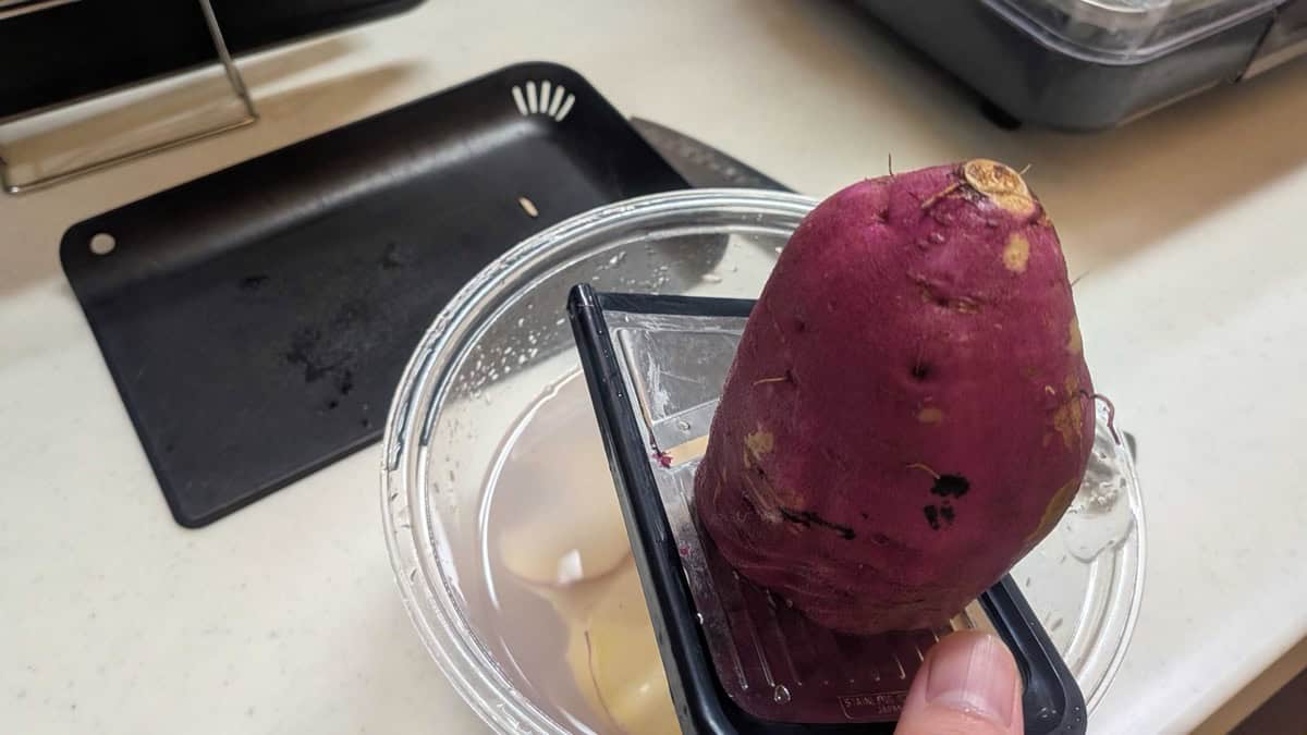 Slicing a Japanese sweet potato on a mandoline directly over a bowl of water
