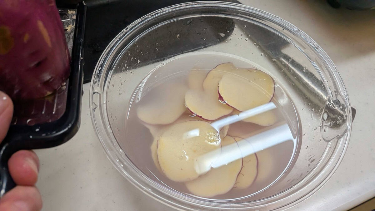 Thin slices of Japanese sweet potato soaking in a glass bowl of water to remove surface starch
