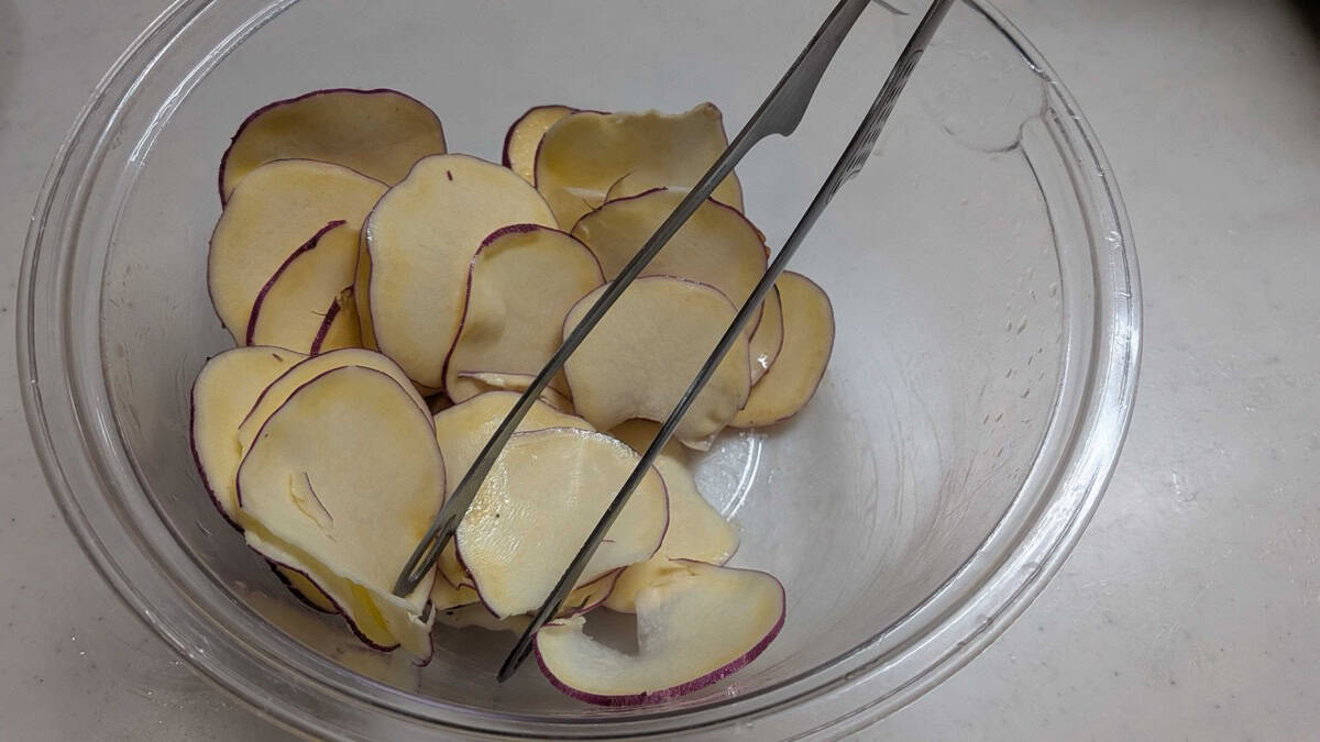 Sweet potato slices being turned gently with tongs in a bowl of melted honey butter