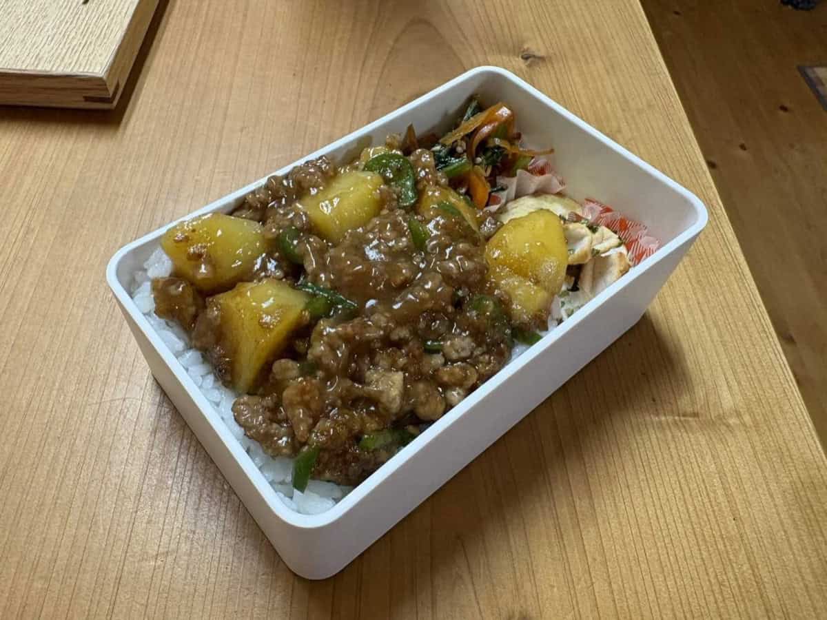 A Japanese bento box with soboro ankake spooned over rice, with namul, tamagoyaki and chicken filling the rest