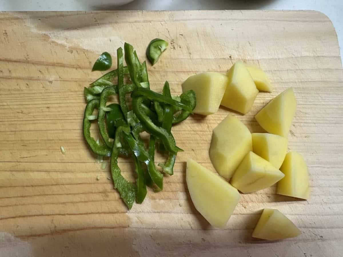 Green pepper cut into strips and potato cut into bite-size chunks on a wooden cutting board