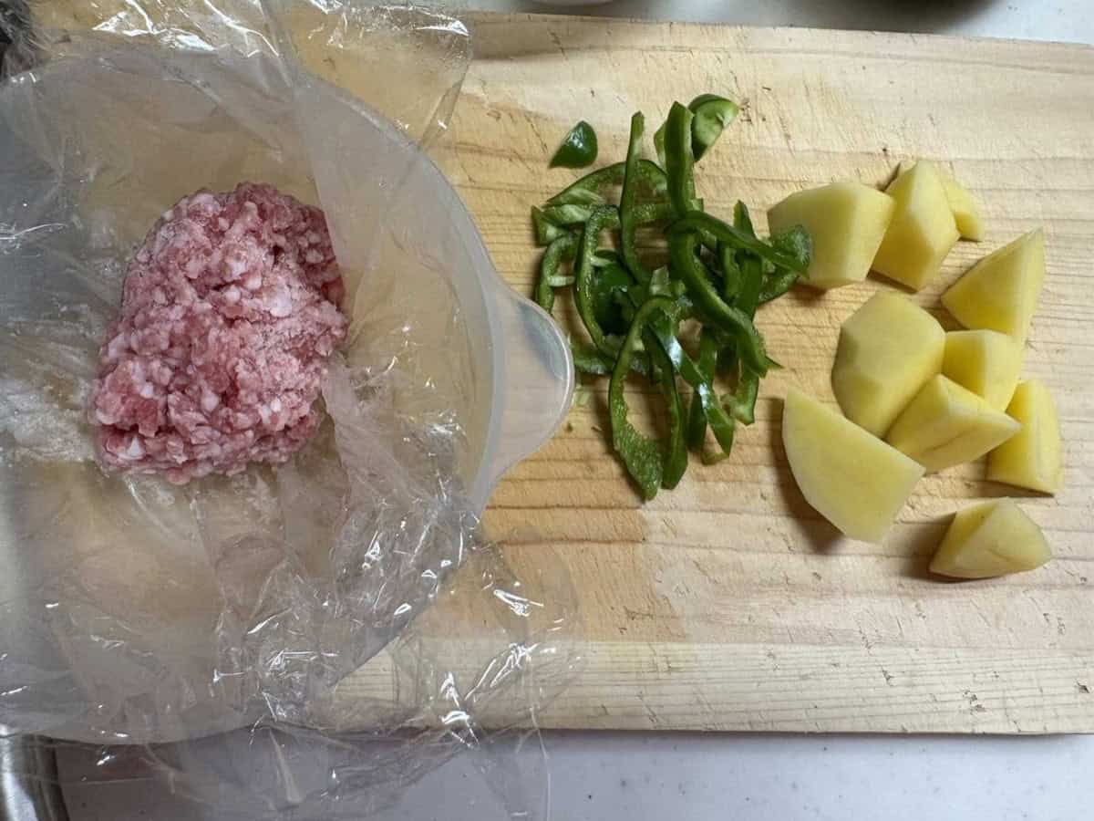 Ground pork in its packet next to sliced green pepper and cut potato on a wooden board