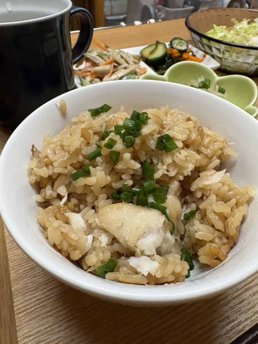 Tai meshi — Japanese sea bream rice with flaked fish and chopped green onion in a white bowl, with side dishes behind