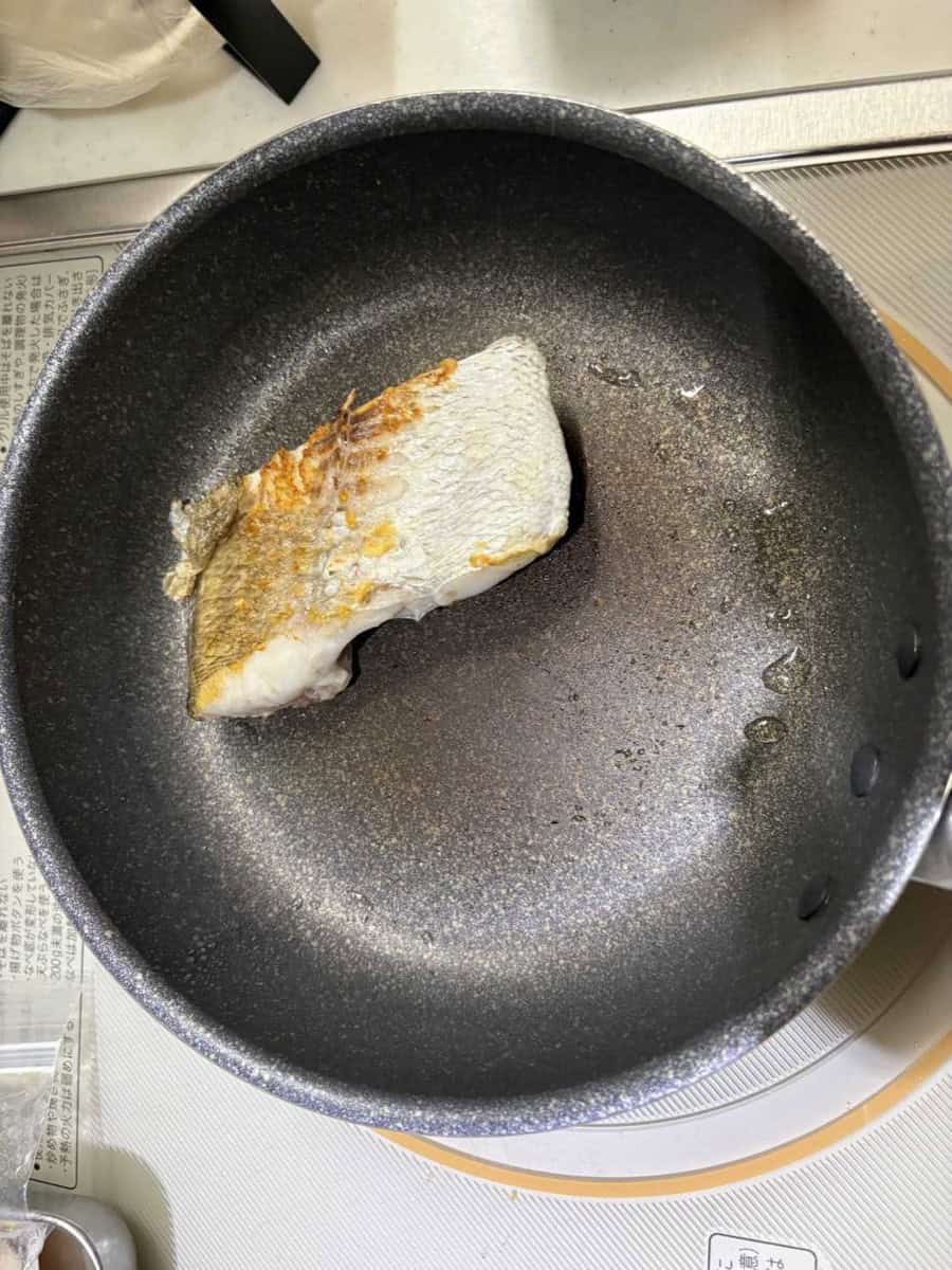 A sea bream fillet with golden seared skin in a nonstick frying pan on an induction stove