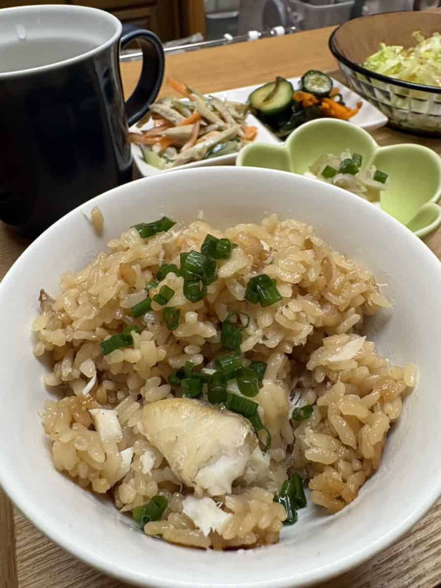 Tai meshi in a white bowl with gobo salad, cucumber pickles, chilled tofu and shredded cabbage on the table behind it