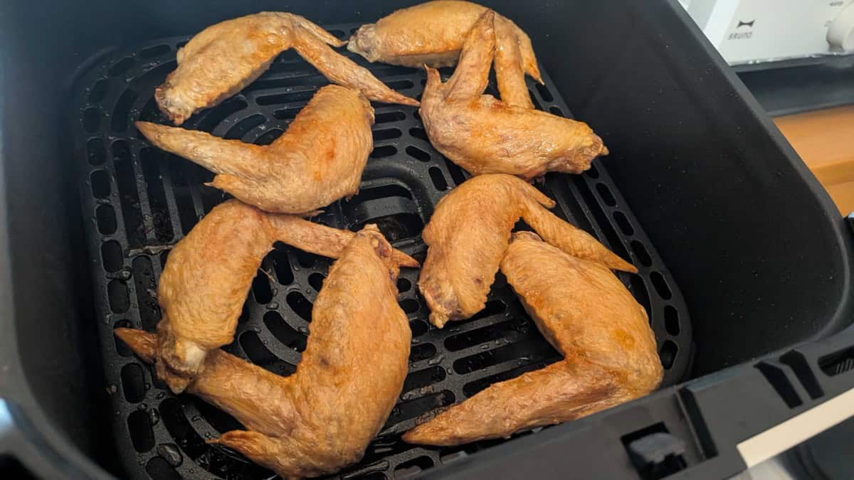 Eight chicken wings in the air fryer basket after cooking, golden brown with crisp tight skin