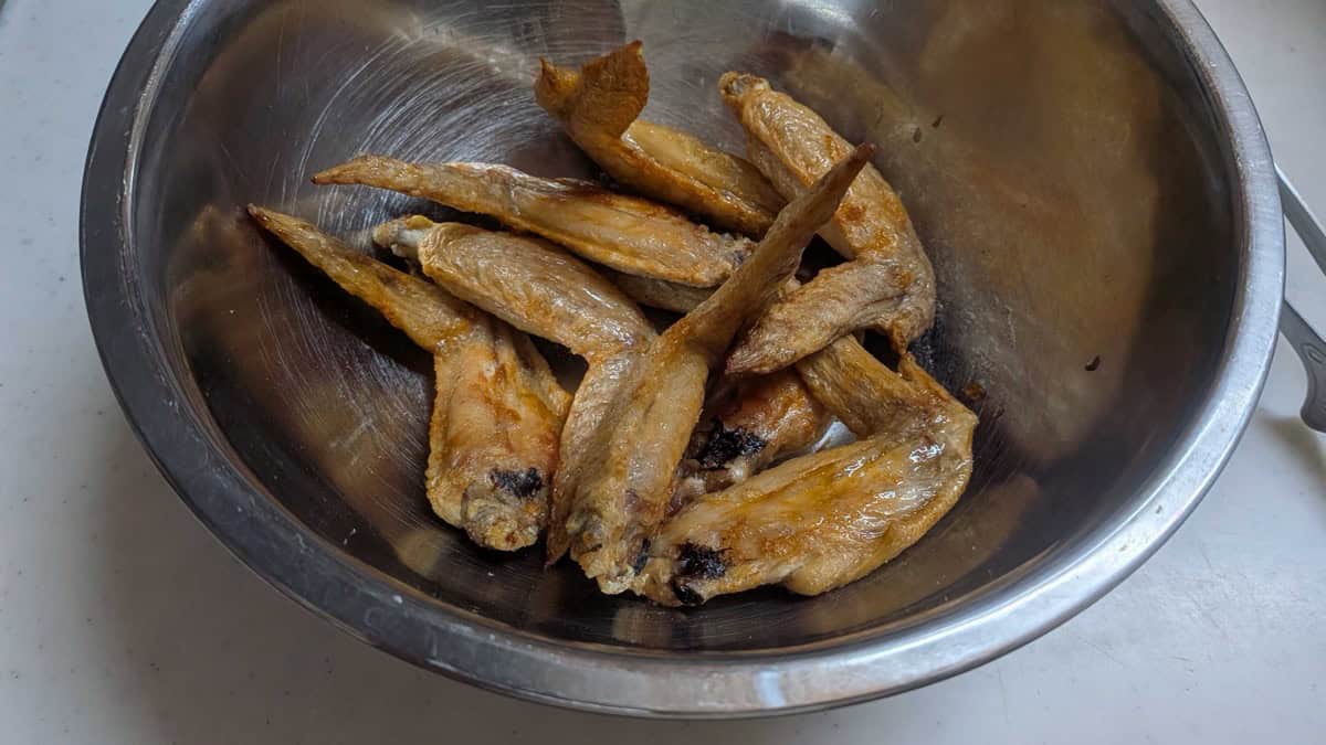 Cooked golden chicken wings tossed with salt and pepper in a stainless steel mixing bowl