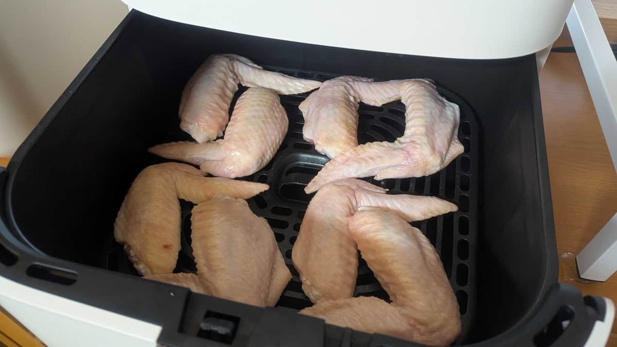 Eight raw seasoned chicken wings arranged in a single layer in an air fryer basket
