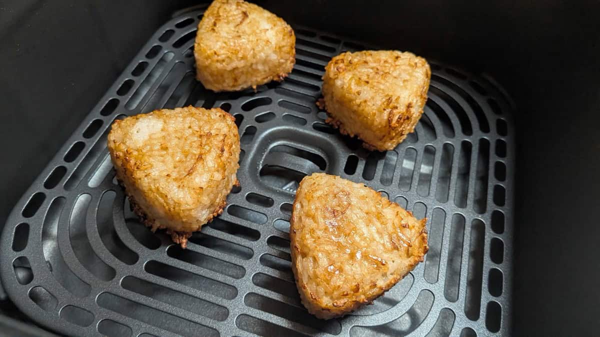 Four yaki onigiri in the air fryer basket after cooking, browned and crisp on every surface