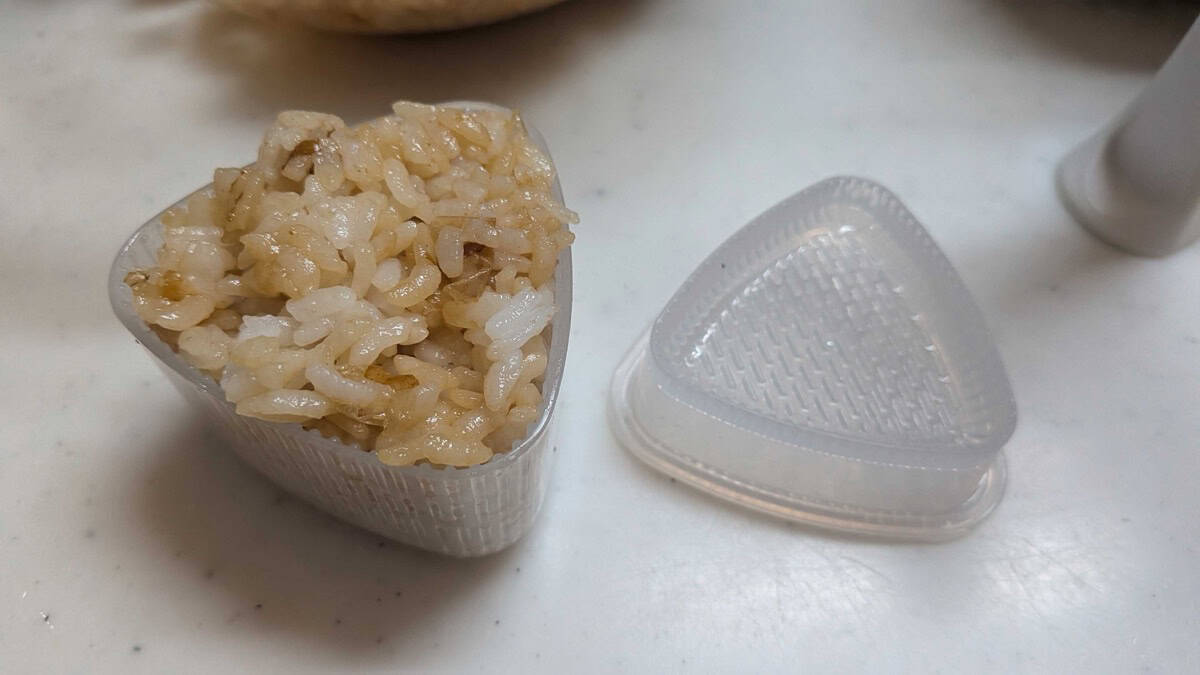 Seasoned rice packed into a plastic triangular onigiri mold with the press lid beside it