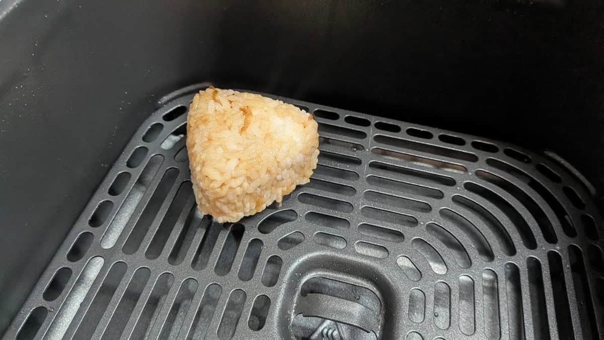 A single shaped yaki onigiri sitting on the air fryer basket tray before cooking